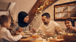 Family enjoying a warm home-cooked meal together at a cozy dining table with festive lights in the background.