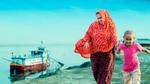 A mother and child from the char (river-island) area walk by, with the Lifebuoy Friendship Hospital in the background